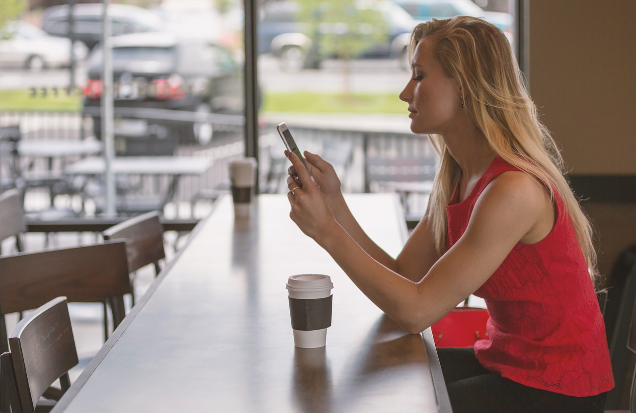 Frau sitzt im Kaffee und schaut auf ihr Smartphone