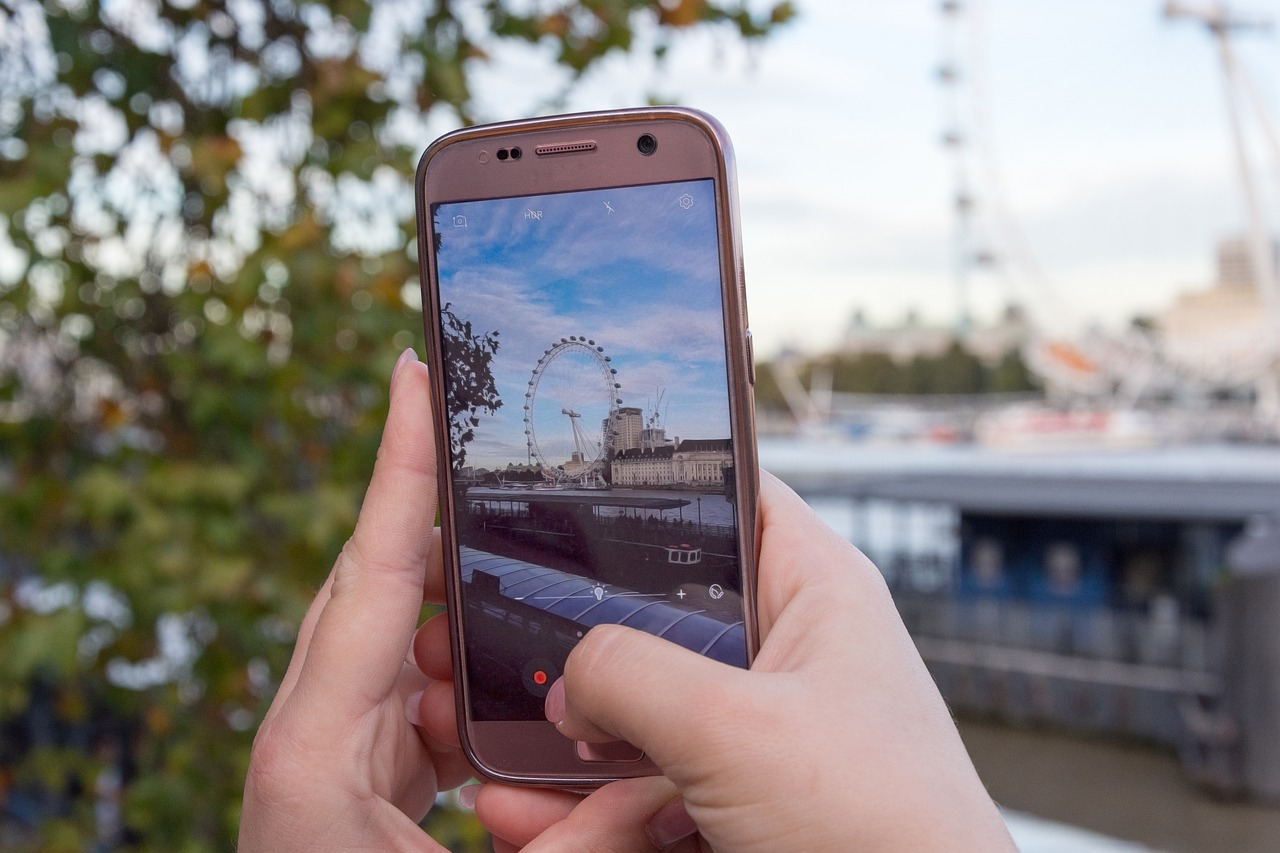 Jemand hält ein Smartphone in der Hand und Fotografiert ein Riesenrad.